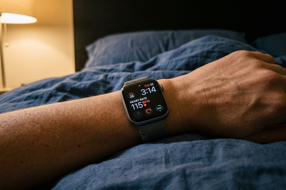 Extreme close-up of a smartwatch on a woman's wrist showing 3:14 AM and elevated heart rate in dim warm bedside light